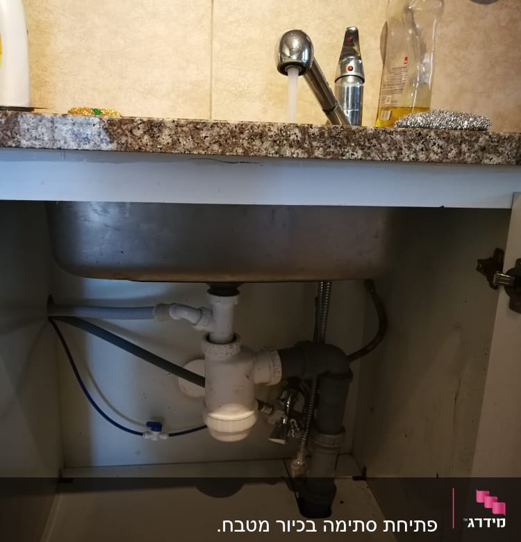 כיור מטבח עם ברז פתוח וצנרת מתחת לכיור